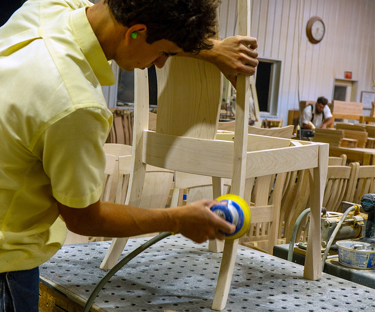 Craftsman sanding a chair frame—handmade quality explaining hardwood furniture lead times in Amish shops.