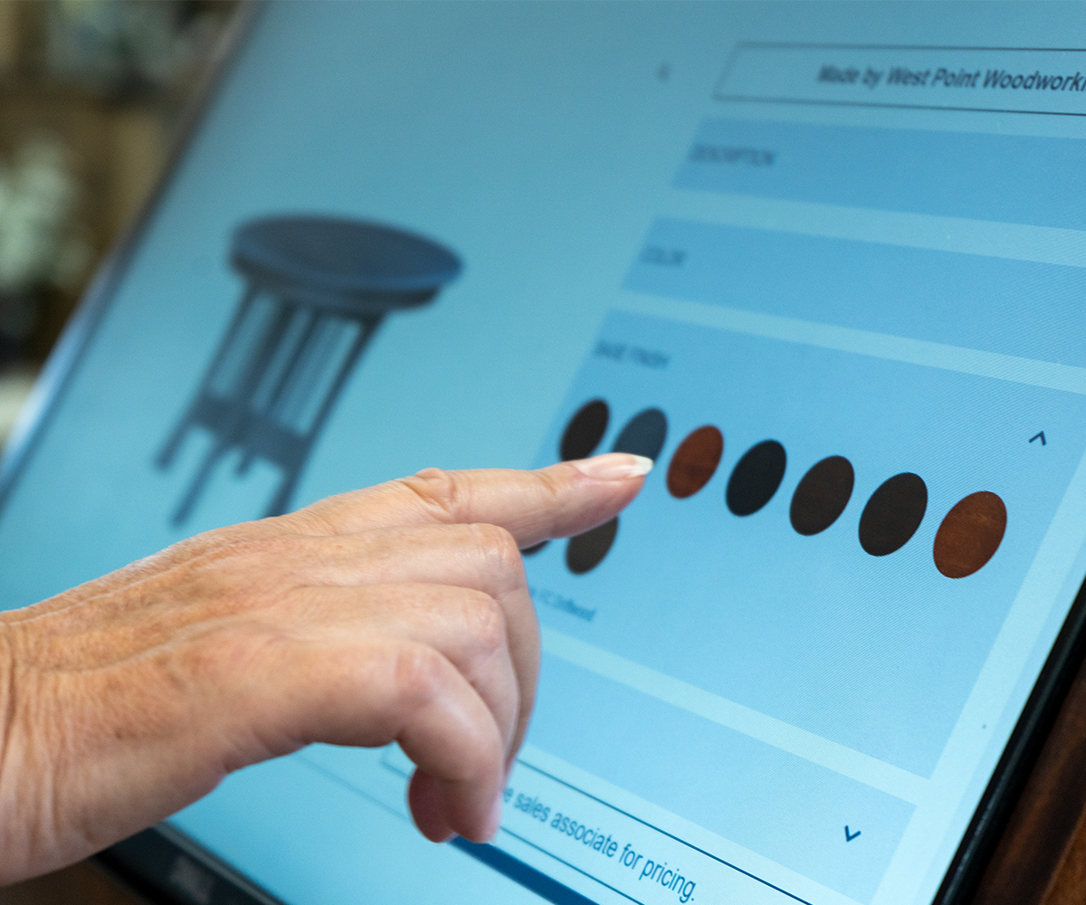 Stacks of raw hardwood planks on a cart in an Amish woodworking shop, with more wood stacks visible in the background.
